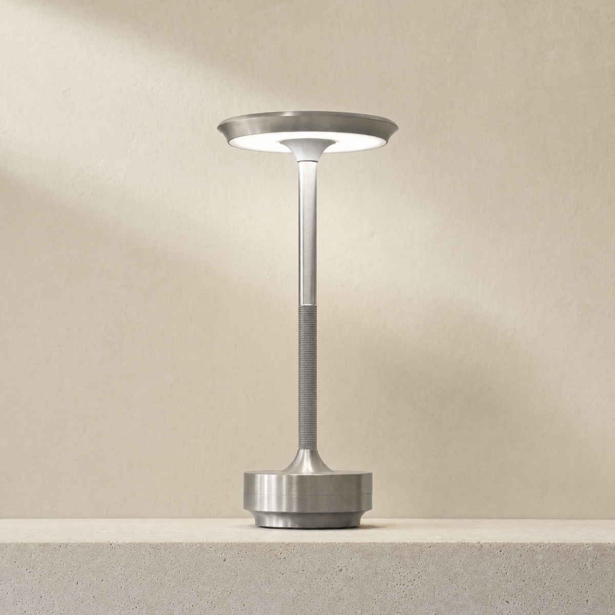 Cordless LED table lamp in silver, lit on a stone ledge